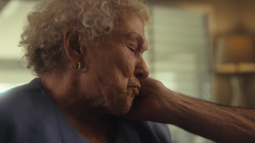 An elderly woman smiling while receiving affection on her face