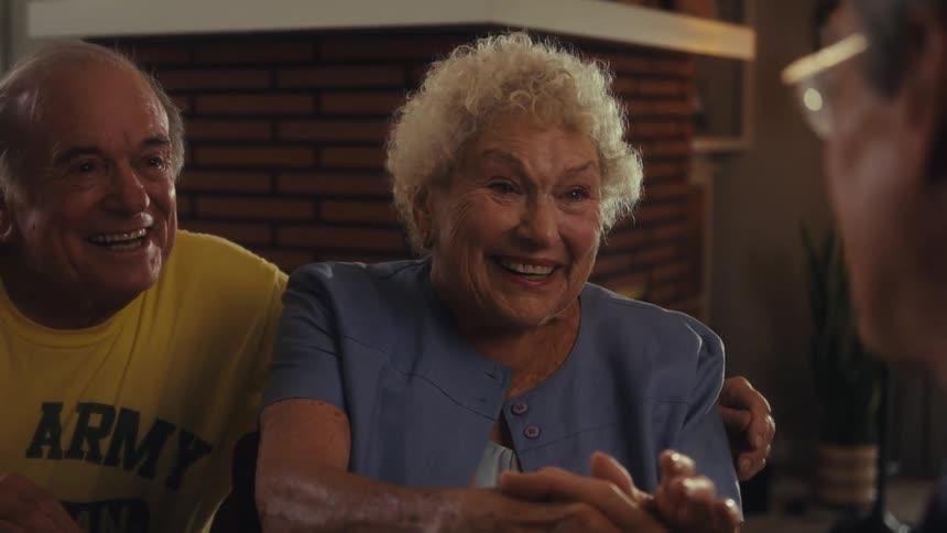 Elderly couple smiles while talking cheerfully with another person