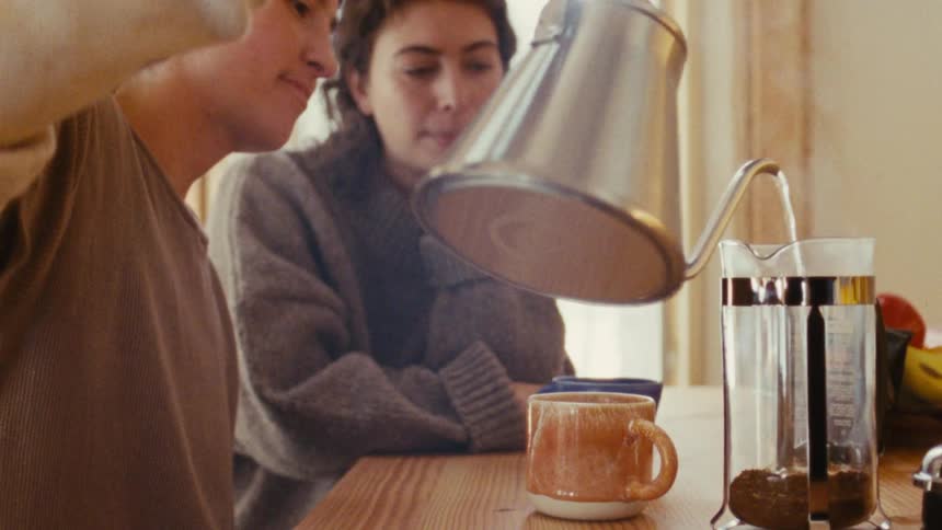 Two people make coffee with a french press at a wooden table