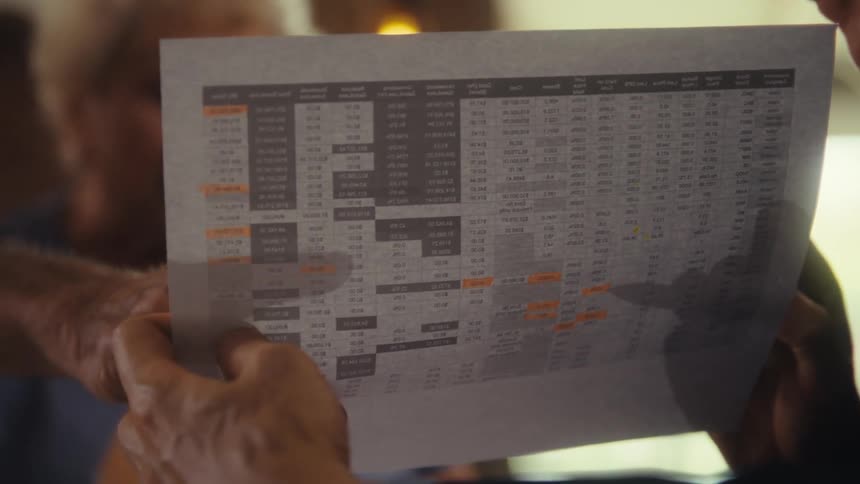 Hands holding a printed spreadsheet with orange highlights