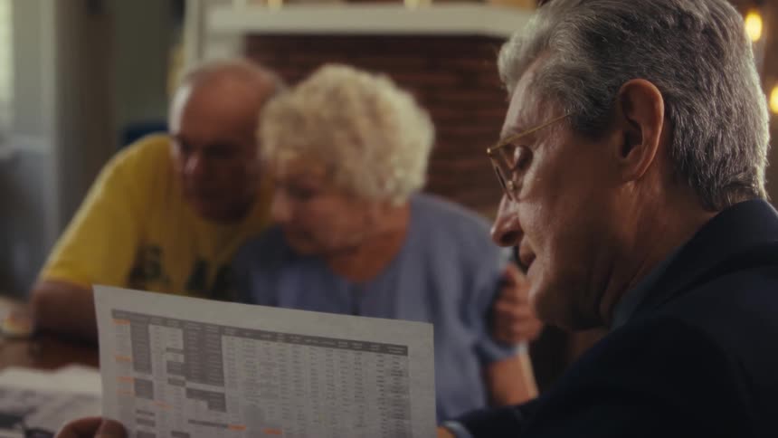 Elderly couple looking at a spreadsheet while a man in a suit and glasses holds it and explains
