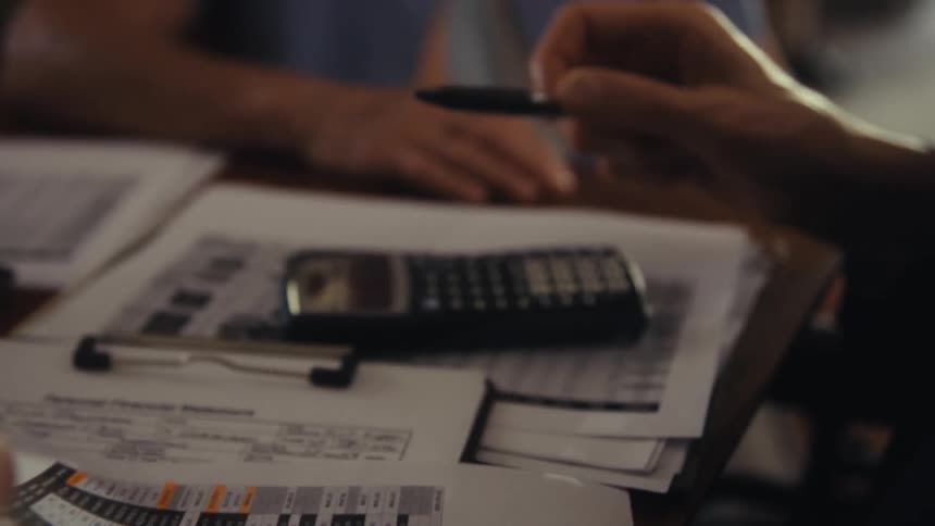 A professional holds a calculator and a pen then sets them down and picks up a sheet of paper to review with an older man and woman