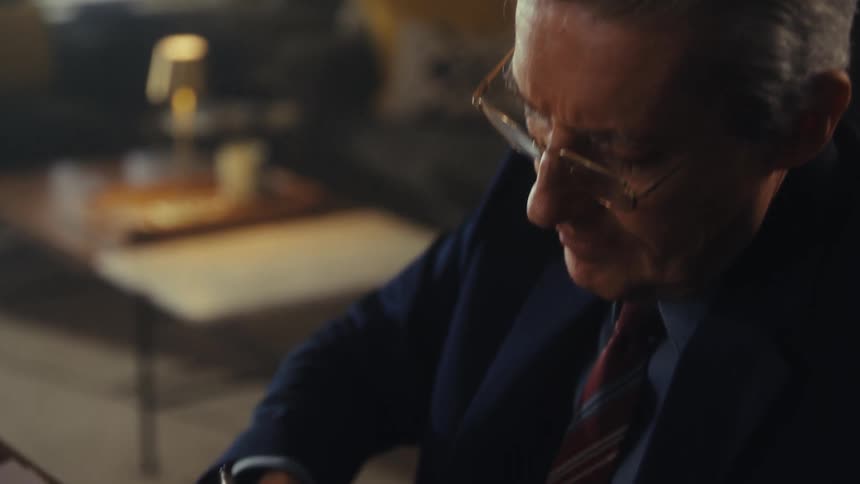 An older man with glasses diligently filling out a form with a pen at a desk