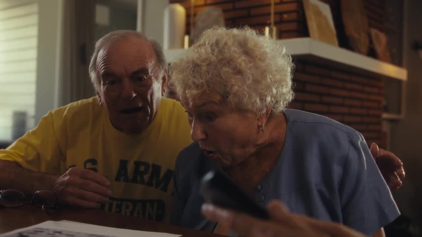 Elderly couple reacts surprised and smiling during conversation with man wearing glasses