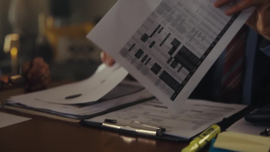 Man in a suit reviews documents while holding a pen