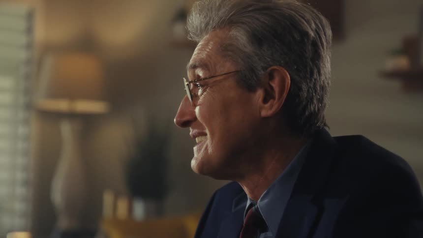 Man in a suit and glasses smiles during a conversation indoors