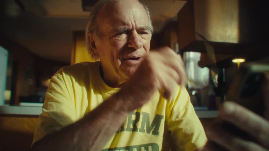 Elderly man smiles while using his phone in a sunlit kitchen