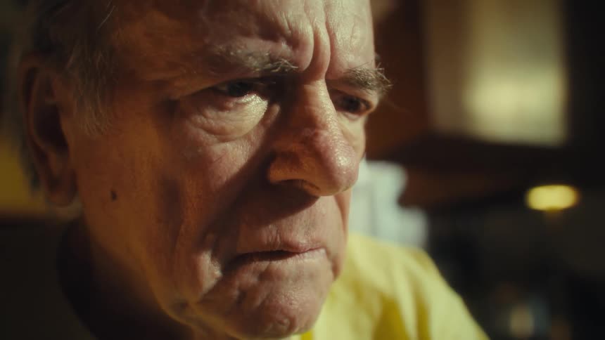 Elderly man reading at home takes off his glasses with a frown