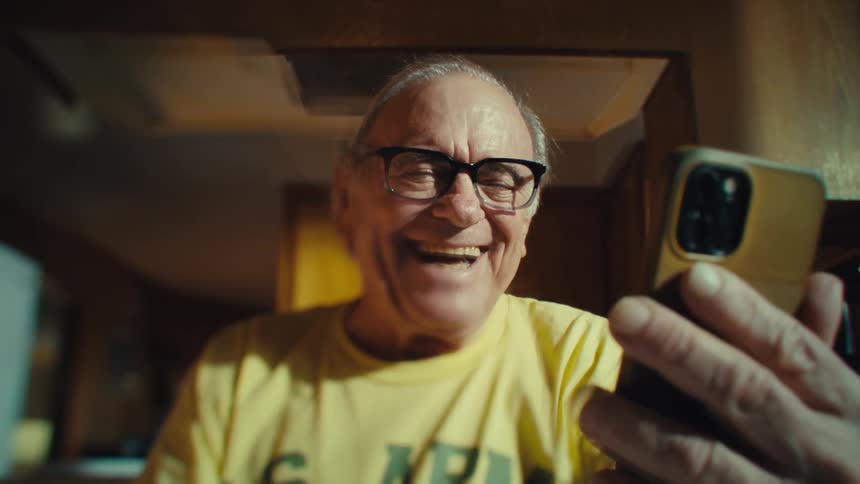 An elderly man joyfully waves while on a video call