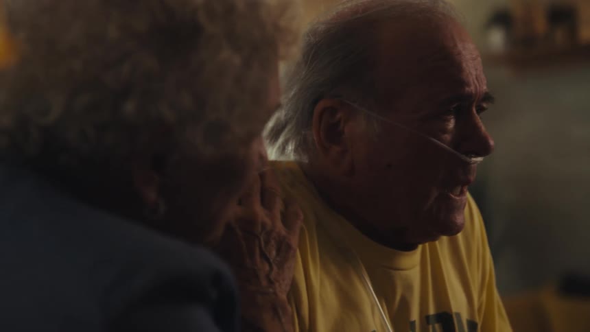 Elderly man with an oxygen tube talking to a woman beside him