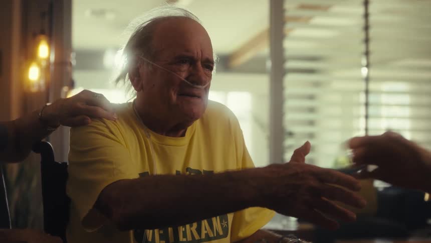A man with an oxygen tube and a yellow tshirt holding hands with a doctor with his wife by his side on a clinic setting