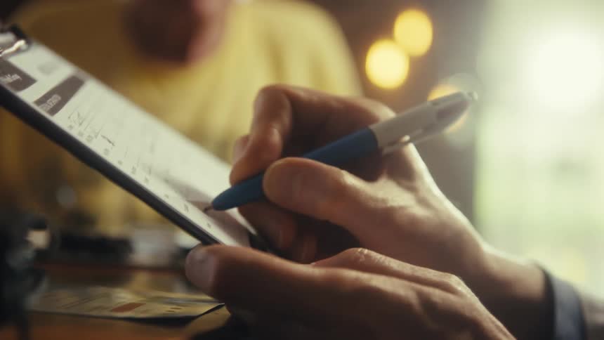 Close up of a doctor filling a patients document on a clipboard while sitting at a table in a room during daytime