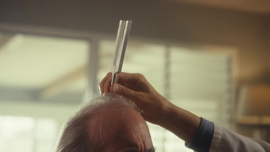 Doctor holds a tuning fork over an elderly patients head