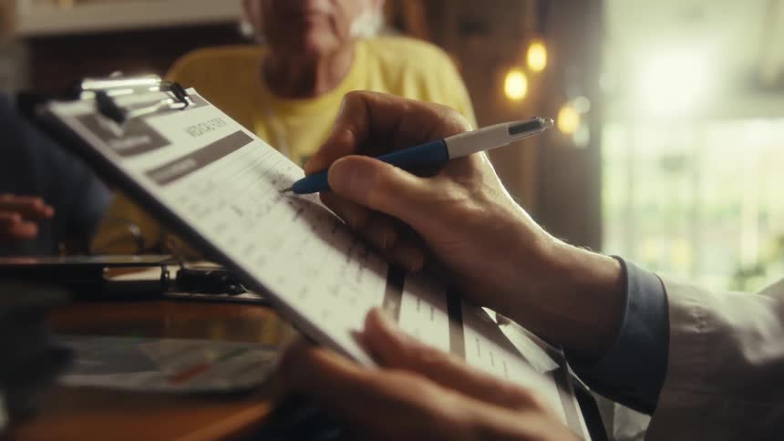 A doctor takes notes as two elderly people speak