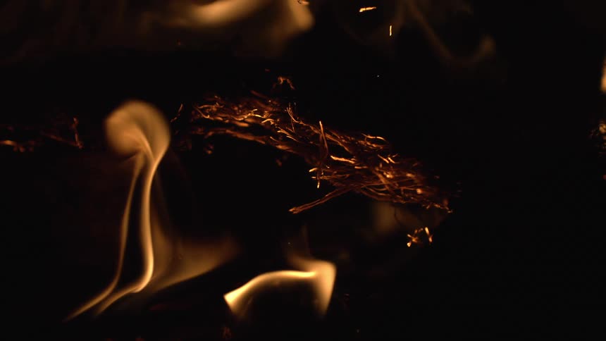 The video shows a closeup shot of embers burning in a fire the warm glowing light of the flames illuminates the scene against a dark background