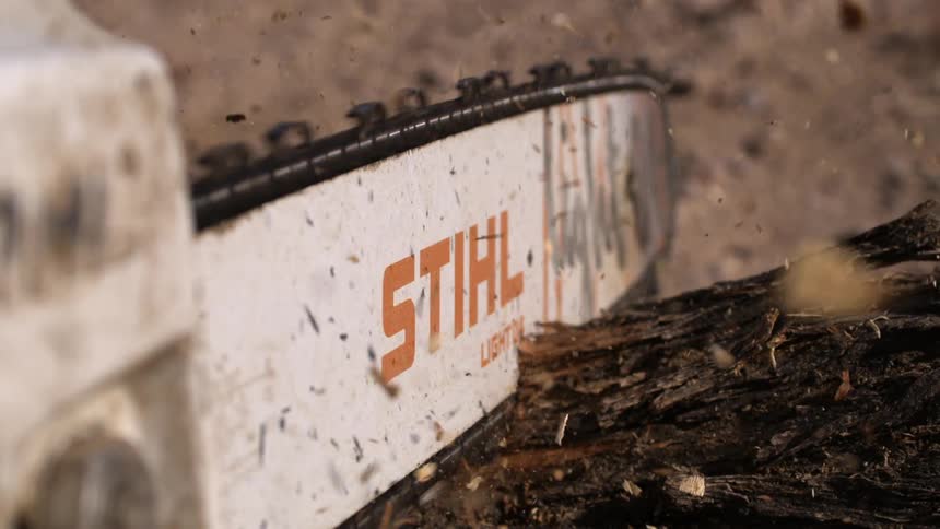 A closeup of a chainsaw with the brand name visible on the side as it cuts through wood causing sawdust to fly