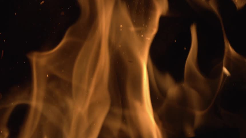 Flames flicker and a few embers arise from a burning fire