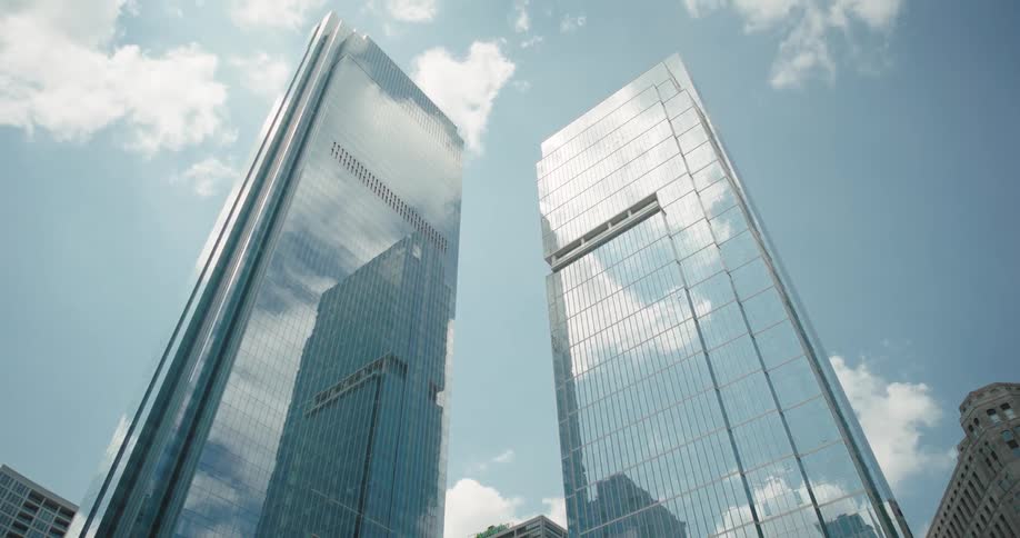 Two skyscrapers in a urban setting with a cloudy and sunny sky in the background