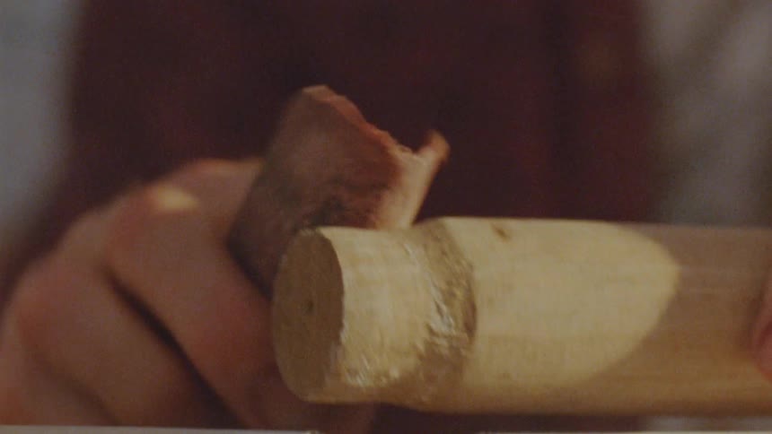 A carpenter is working on a piece of wood using sandpaper to smooth the surface so it fits into an opening on another piece of wood