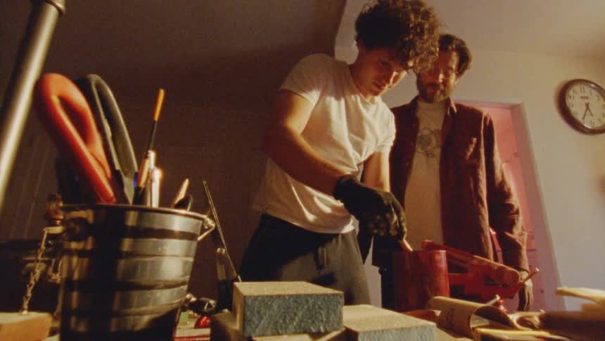Two men are working together at a cluttered workbench indoors