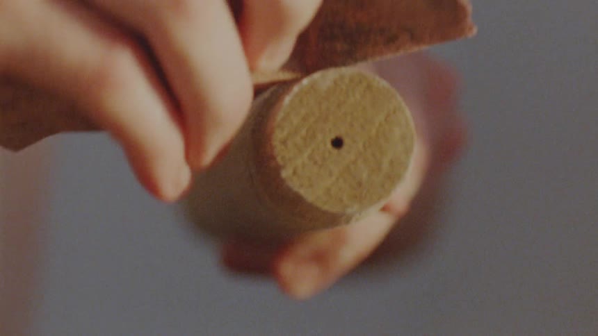 A person holds a wooden dowel steady as it is shaped with a piece of sand paper