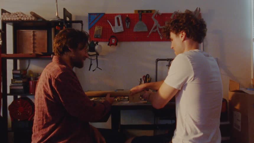 Two men are sanding a piece of wood in a workshop
