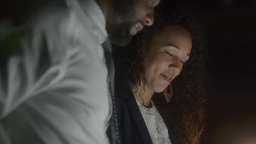 Woman smiling while looking down next to a man in a dimly lit setting