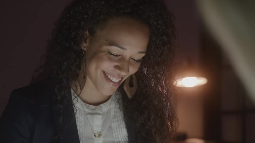 Woman smiling softly while looking down in a room lit by a lamp