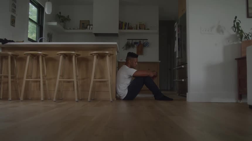 A young man sits on the kitchen floor looking distressed