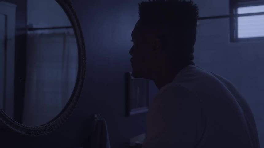 Man looks at his reflection in a round mirror in a dimly lit room