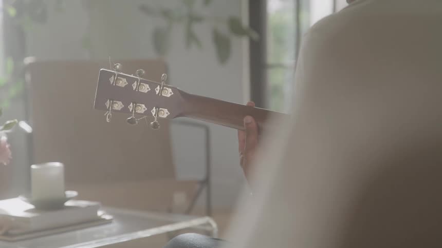 Person plays guitar in a room lit by natural light