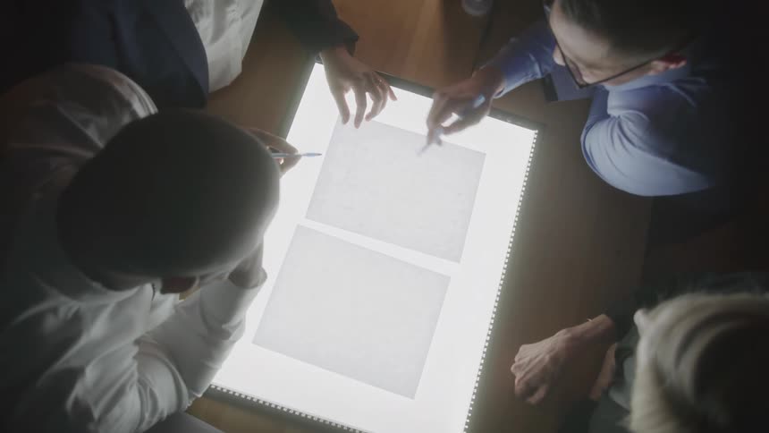 Group of people discusses documents on a lit light table