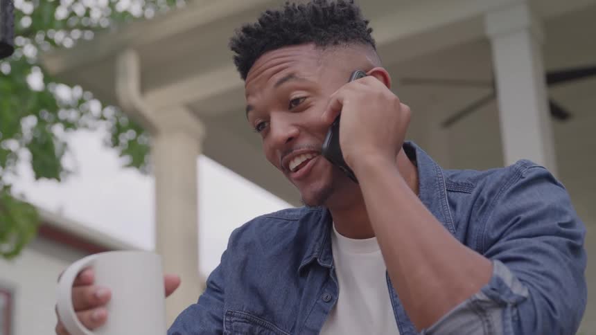 Man smiling while on the phone and holding a coffee mug