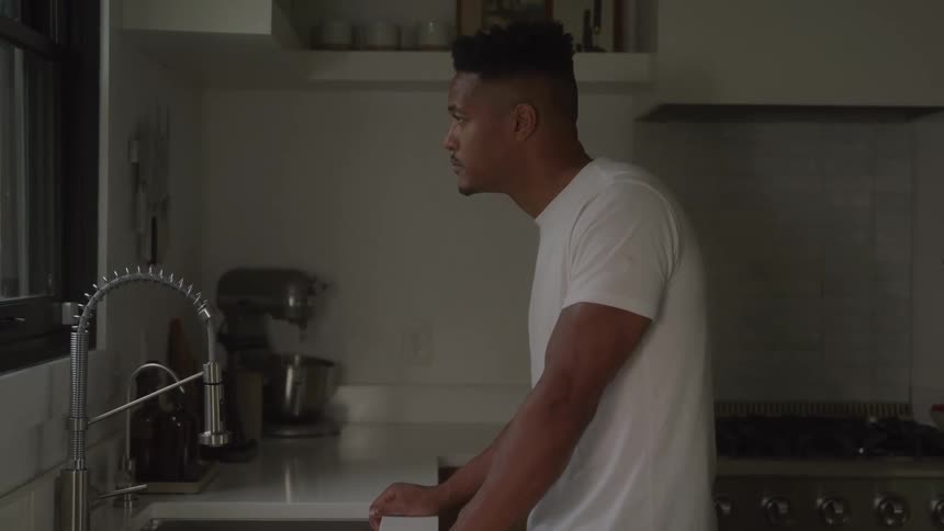A man leans over a kitchen counter thoughtfully
