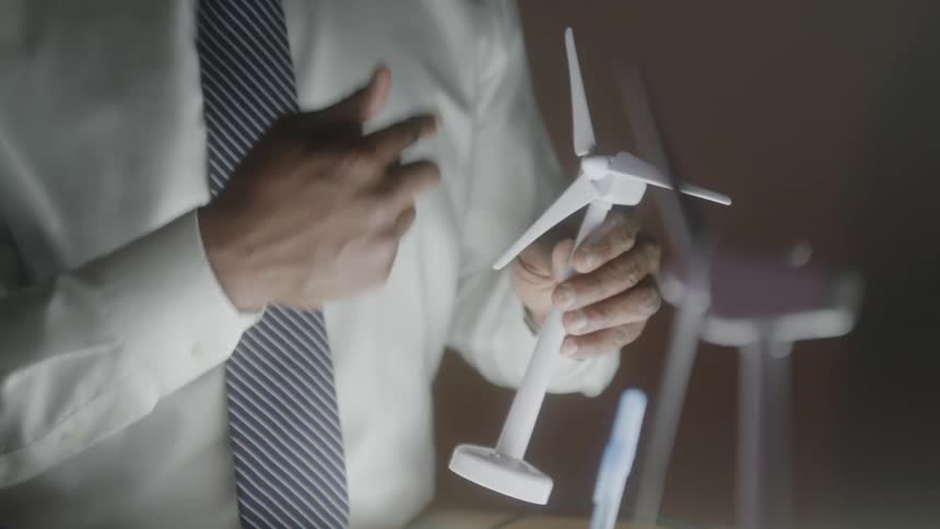 A man holds a model windmill and points to it