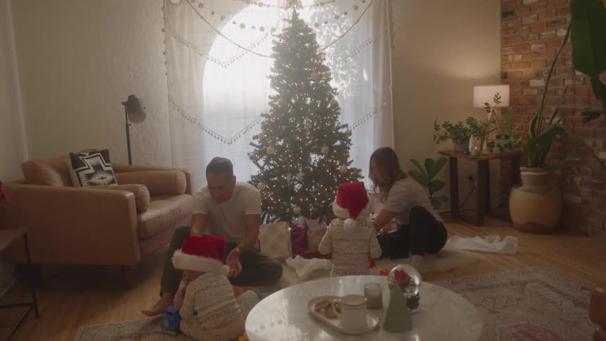 Family gathered in front of the christmas tree while children play wearing red hats