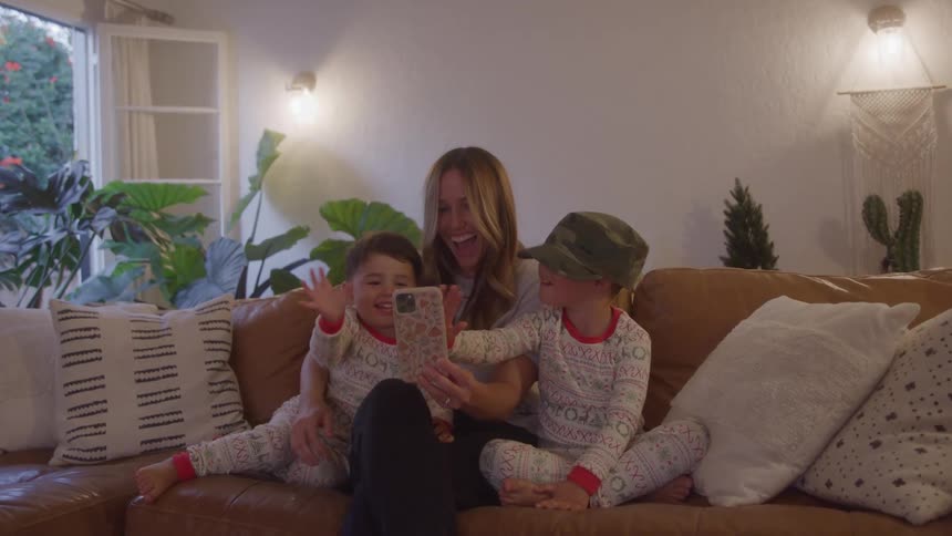 Mother and kids wave on video call in living room