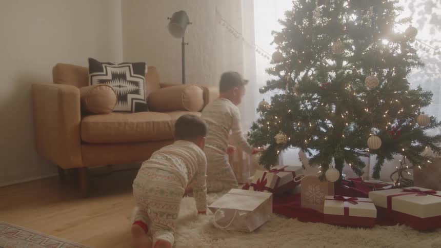 Two kids look excitedly at christmas presents under the tree