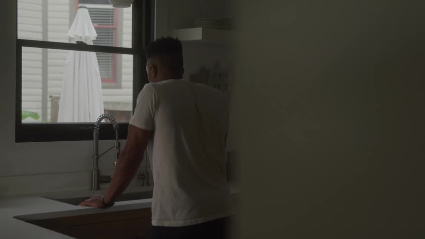 A man stands at a kitchen sink looking out the window