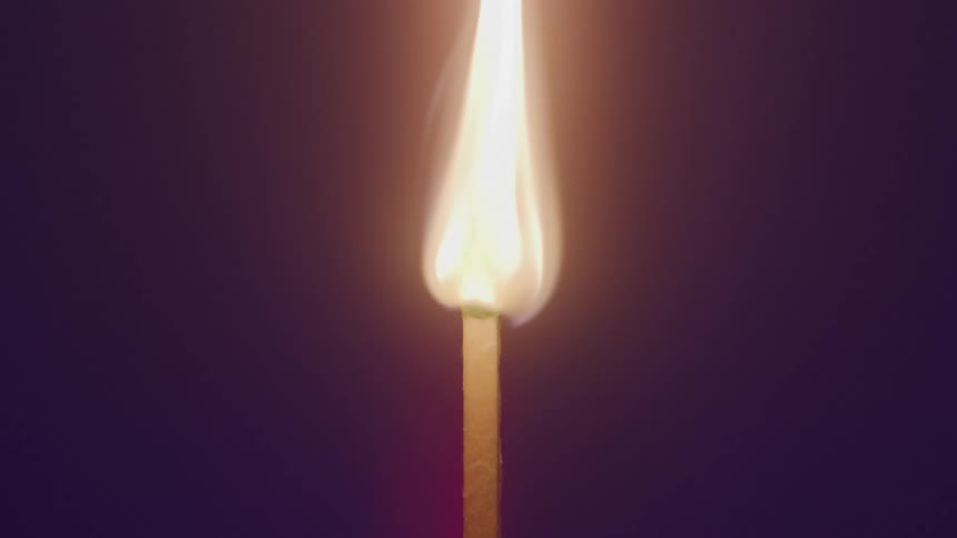 Lit matchstick burning against a dark background