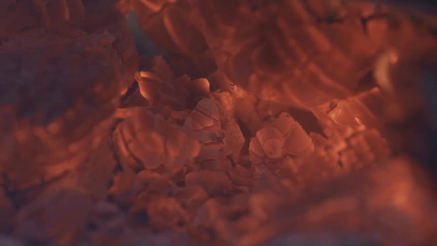A glowing cluster of red and orange embers burns intensely as they shift and smolder in the center of a pile of ash and dark rubble