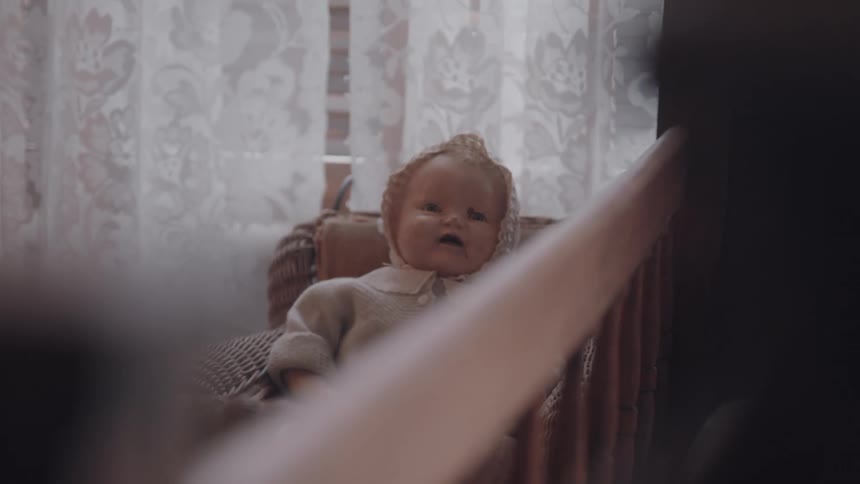 Doll in a room of the house next to a window with a white curtain