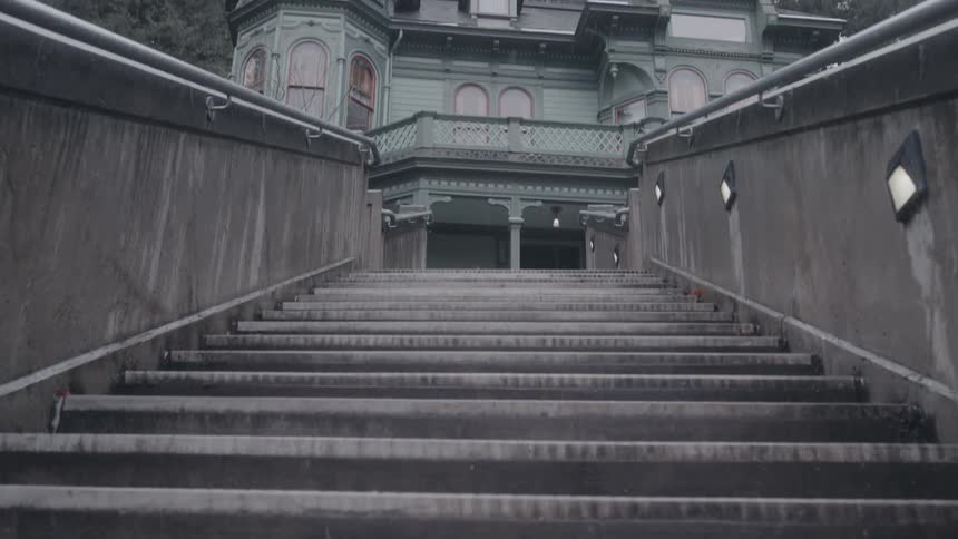 Concrete staircase leading to a greenishgray victorian mansion surrounded by trees