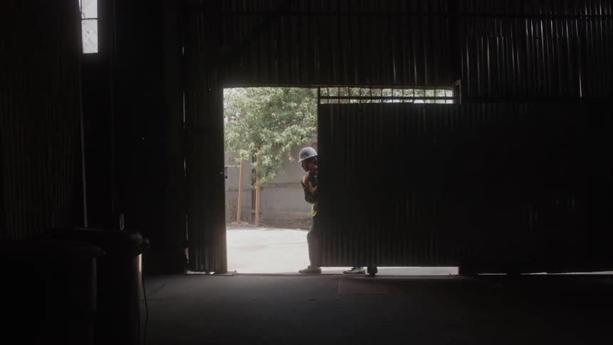 Worker with helmet and reflective vest closing the metal gate of a warehouse