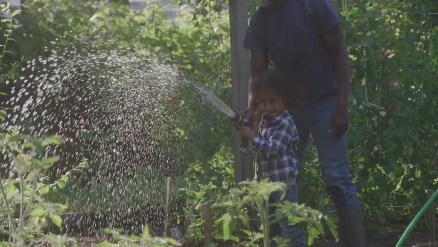 Father and son water the garden together with a hose