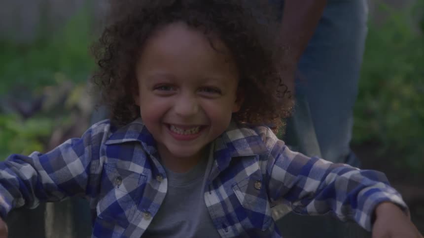 The child is smiling while being pushed in the wheelbarrow