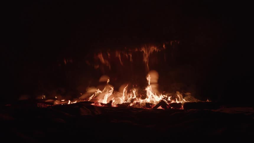 Logs of wood burn in a fire on an open field at night