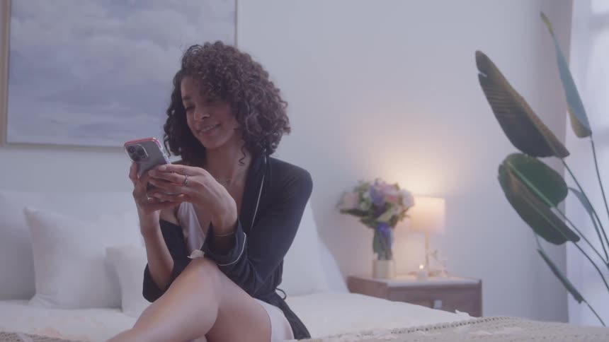 A woman is smiling while texting on her phone