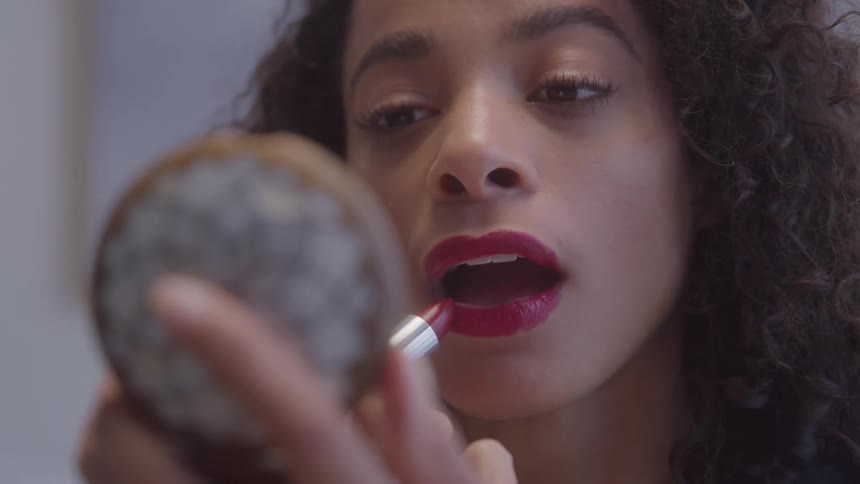 Woman applying red lipstick while looking into a handheld mirror