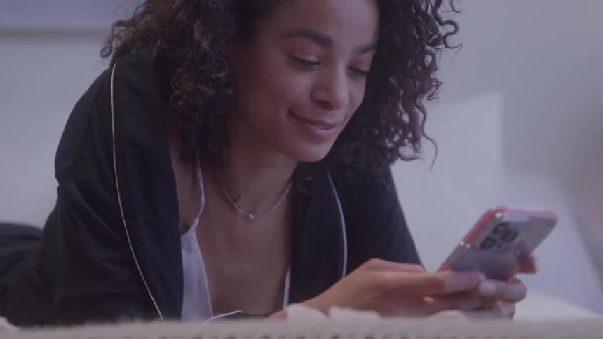 The woman lays on the bed texting